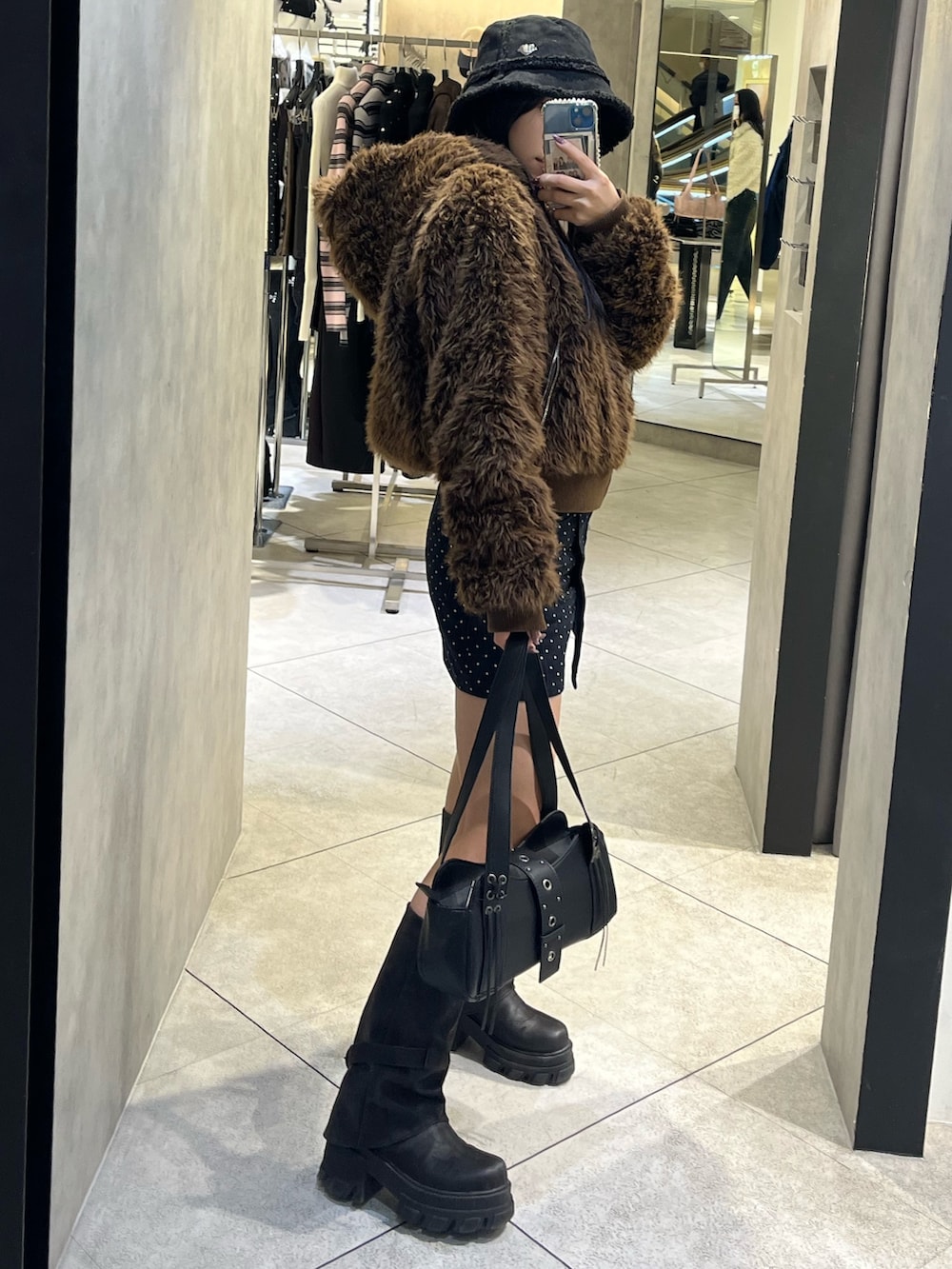 ブラック系のブーツ、ブラック系のハンドバッグ、ブルー系のスカートを着用したレディースの秋コーディネートの2枚目の写真