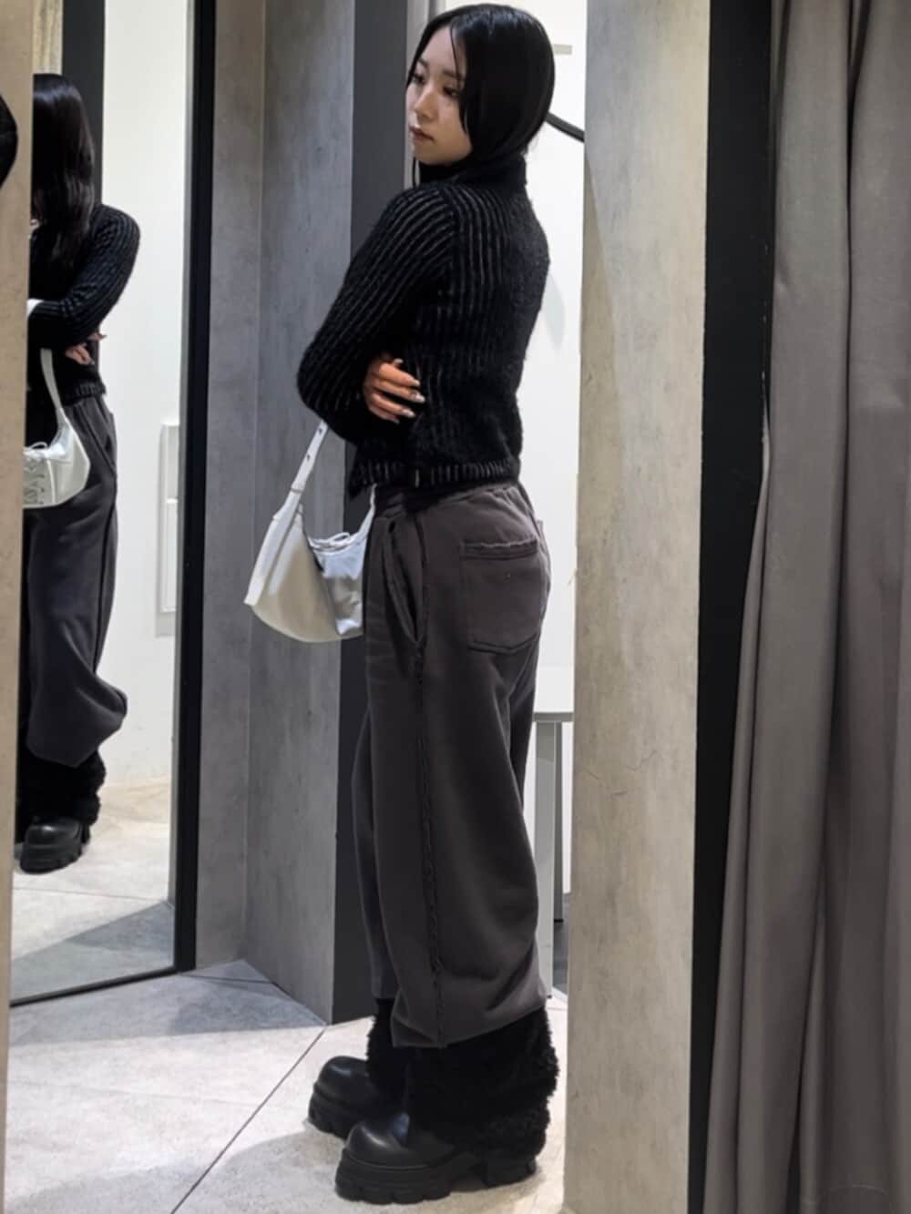 ブラック系のニット/セーター、ホワイト系のショルダーバッグ、ブラック系のブーツを着用したレディースの冬コーディネートの2枚目の写真