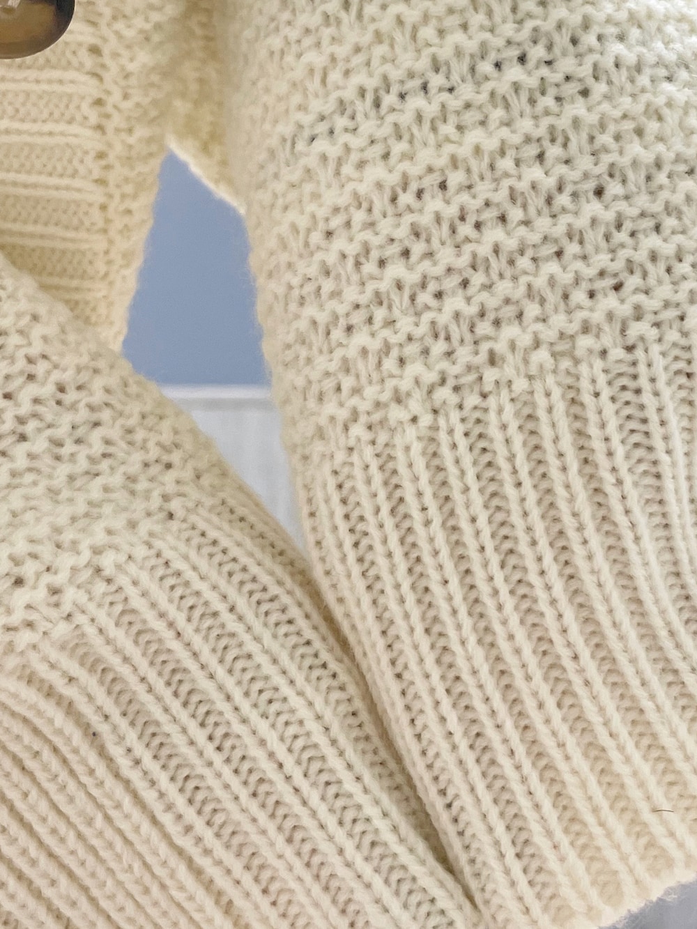 ホワイト系のショルダーバッグ、ホワイト系のカーディガン/ボレロ、ブルー系のデニムパンツを着用したレディースの冬コーディネートの5枚目の写真