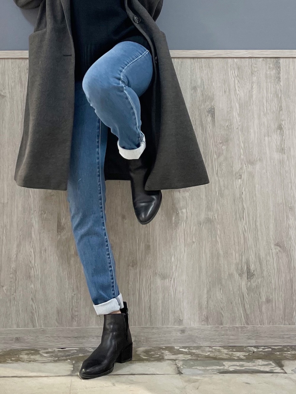 グレー系のチェスターコート、ブルー系のデニムパンツ、ブラック系のニット/セーターを着用したレディースの冬コーディネートの2枚目の写真