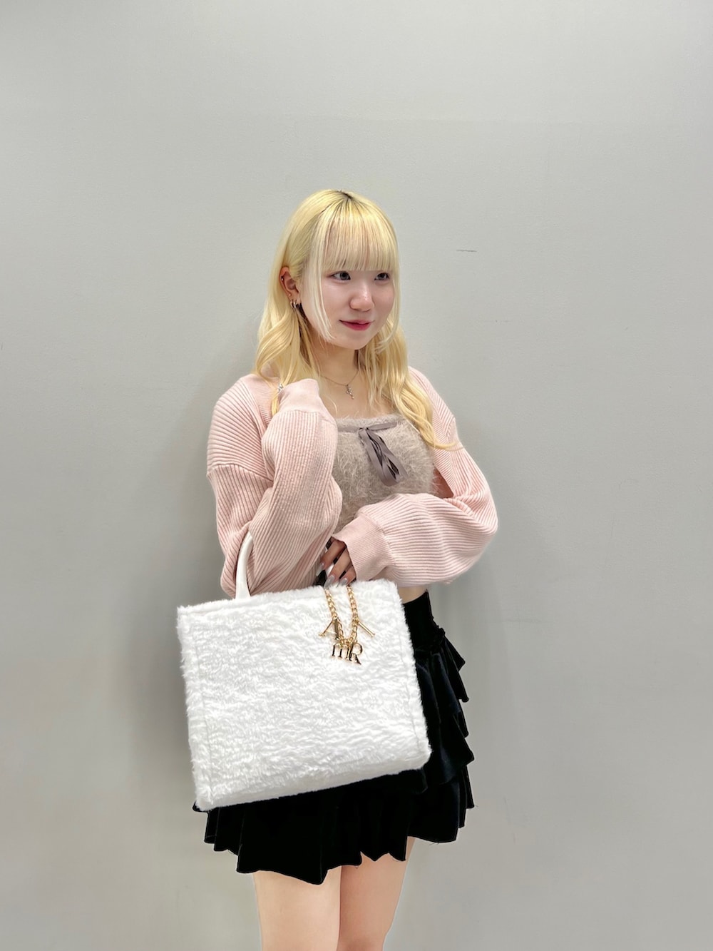 ホワイト系のトートバッグ、ピンク系のアンサンブル、ブラック系のスカートを着用したレディースの秋コーディネートの3枚目の写真