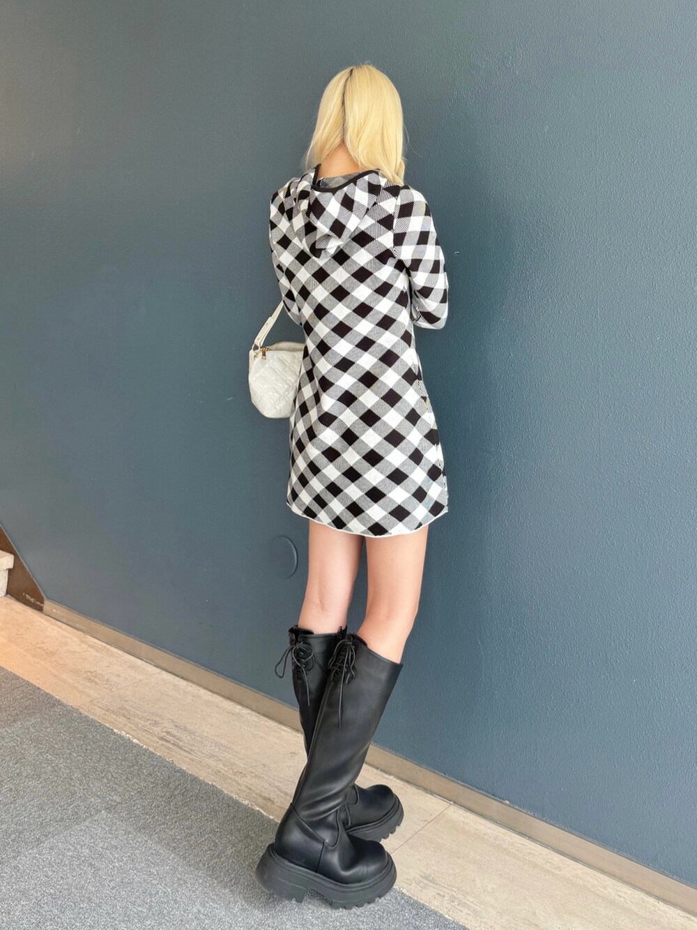 ブラック系のワンピース、ホワイト系のショルダーバッグ、ブラック系のブーツを着用したレディースの秋コーディネートの2枚目の写真