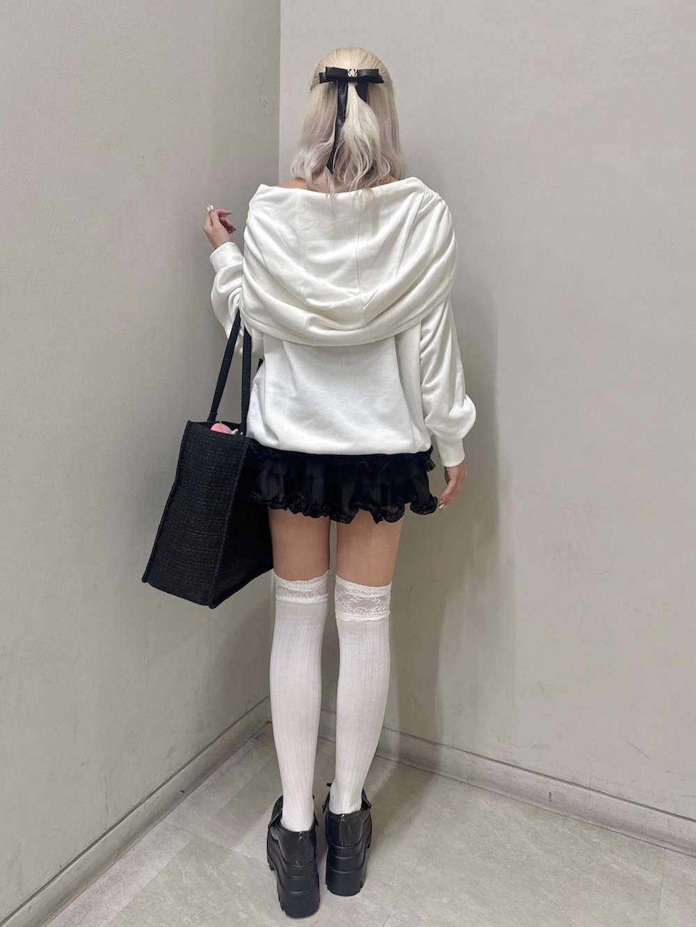 ホワイト系のパーカー、ブラック系のトートバッグ、ブラック系のスカートを着用したレディースの春コーディネートの3枚目の写真