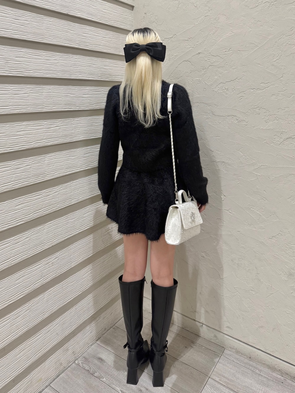 ブラック系のセットアップ、ホワイト系のショルダーバッグ、ブラック系のブーツを着用したレディースの冬コーディネートの3枚目の写真