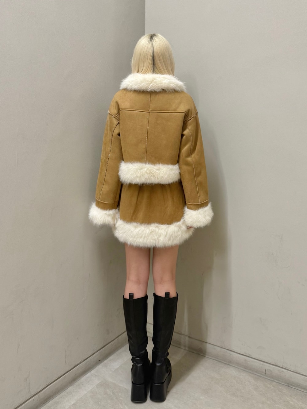 イエロー系のムートンコート、イエロー系のスカート、ブラック系のブーツを着用したレディースの秋コーディネートの2枚目の写真