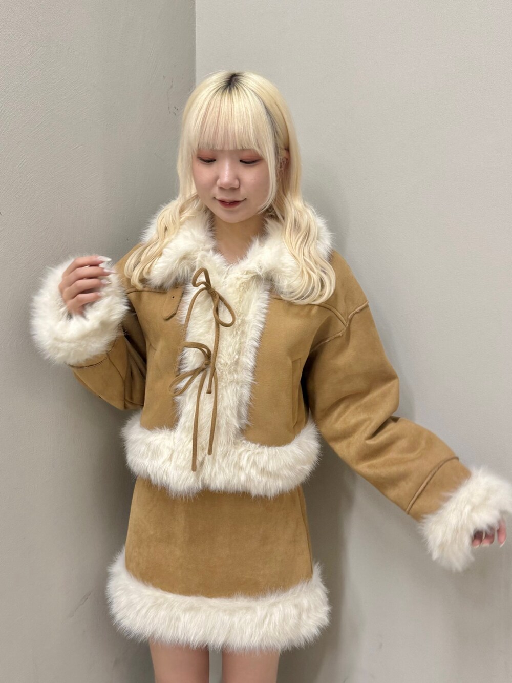 イエロー系のムートンコート、イエロー系のスカート、ブラック系のブーツを着用したレディースの秋コーディネートの3枚目の写真