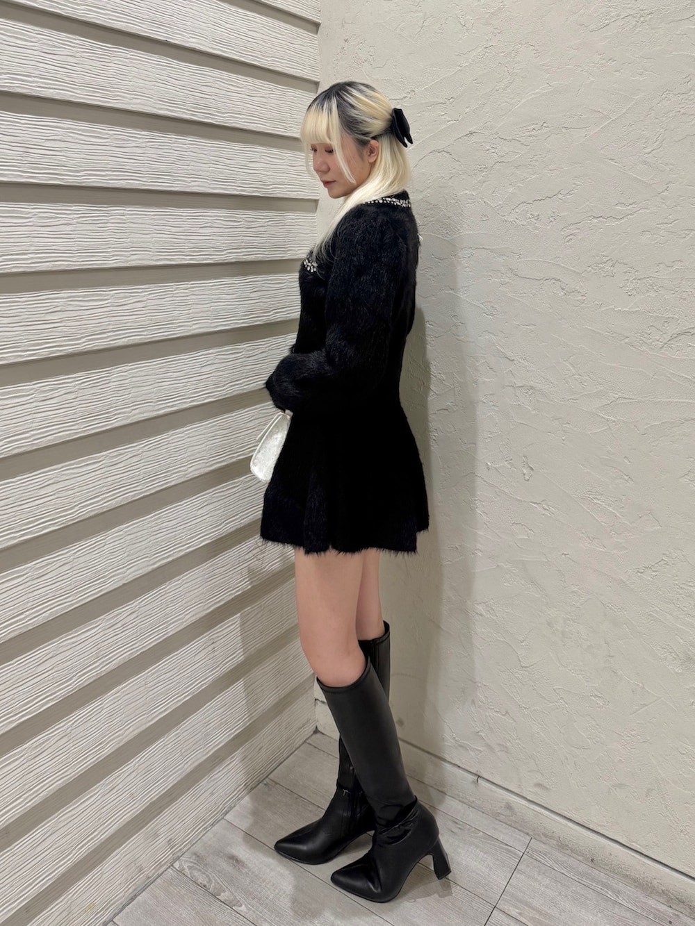 ブラック系のセットアップ、ホワイト系のショルダーバッグ、ブラック系のブーツを着用したレディースの冬コーディネートの2枚目の写真