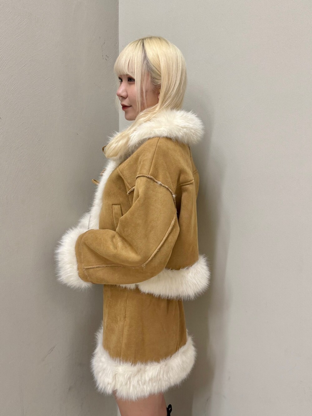 イエロー系のムートンコート、イエロー系のスカート、ブラック系のブーツを着用したレディースの秋コーディネートの4枚目の写真