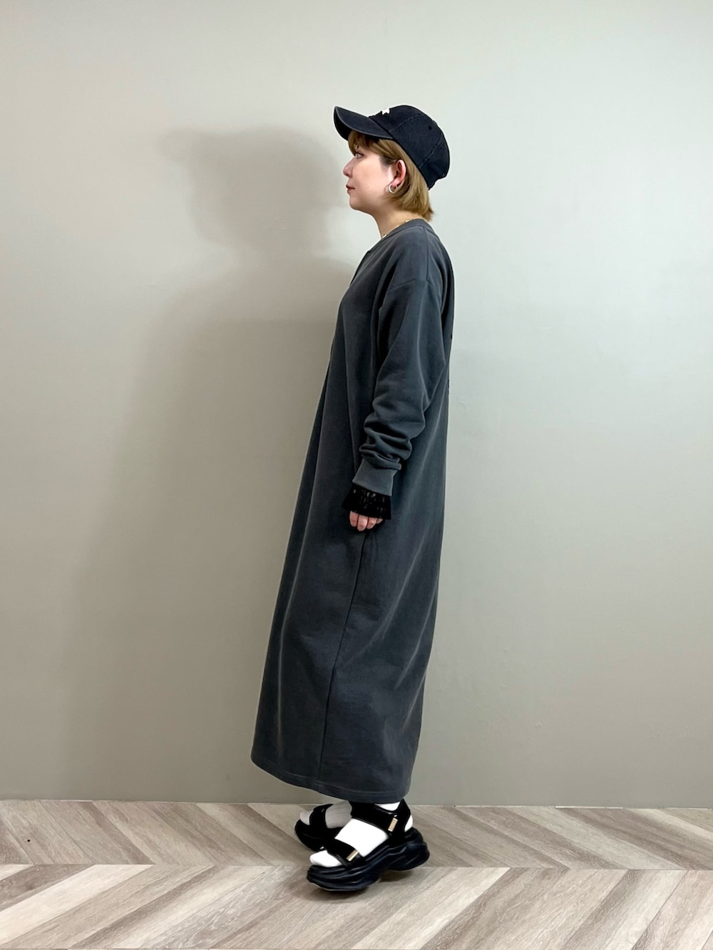 グレー系のワンピース、ブラック系のTシャツ/カットソー、ゴールド系のネックレスを着用したレディースの春コーディネートの2枚目の写真