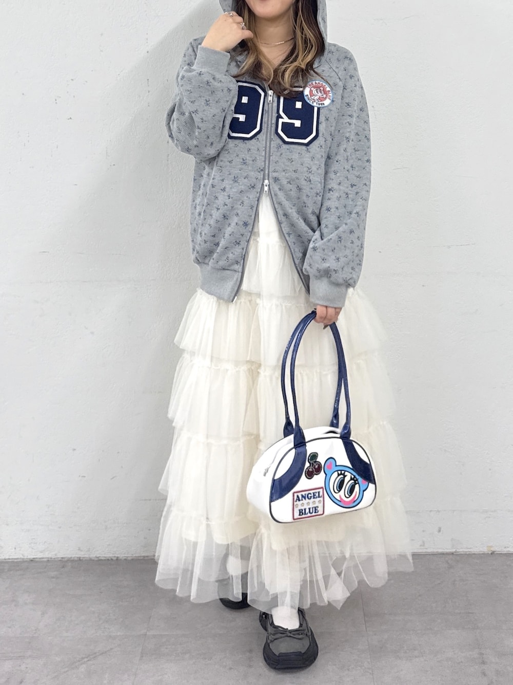 グレー系のパーカー、ブルー系のボストンバッグ、ホワイト系のジャンパースカートを着用したレディースの春コーディネートの2枚目の写真