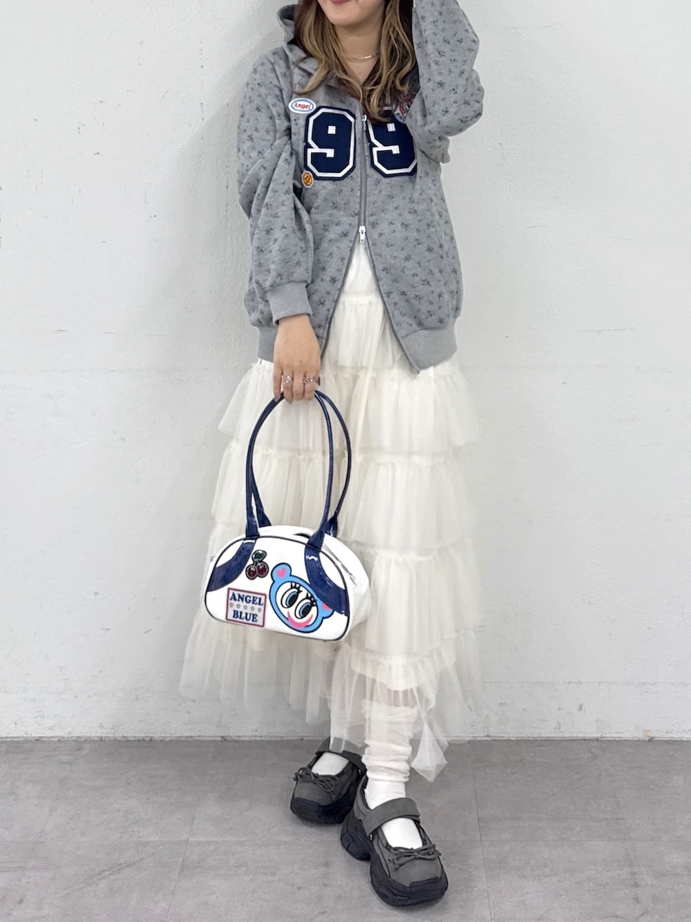 グレー系のパーカー、ブルー系のボストンバッグ、ホワイト系のジャンパースカートを着用したレディースの春コーディネートの3枚目の写真