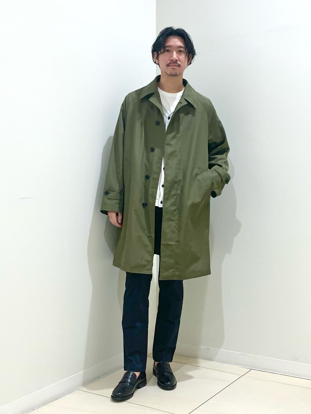 グリーン系のステンカラーコート、ブルー系のチノパンツ、グレー系のカーディガン/ボレロを着用したメンズの春コーディネートの2枚目の写真