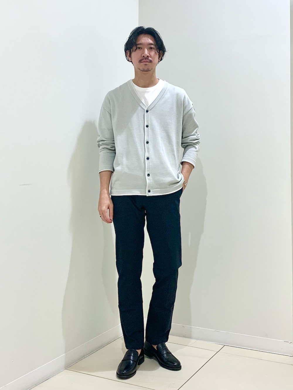 グリーン系のステンカラーコート、ブルー系のチノパンツ、グレー系のカーディガン/ボレロを着用したメンズの春コーディネートの3枚目の写真