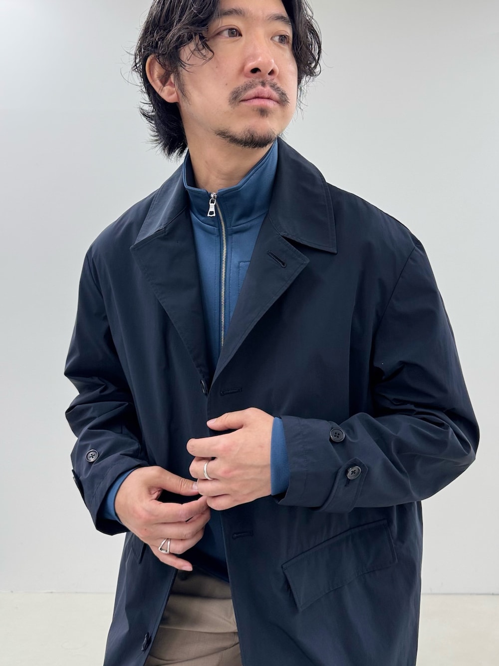 ブルー系のブルゾン、ブルー系のステンカラーコート、ベージュ系のスラックスを着用したメンズの春コーディネートの4枚目の写真