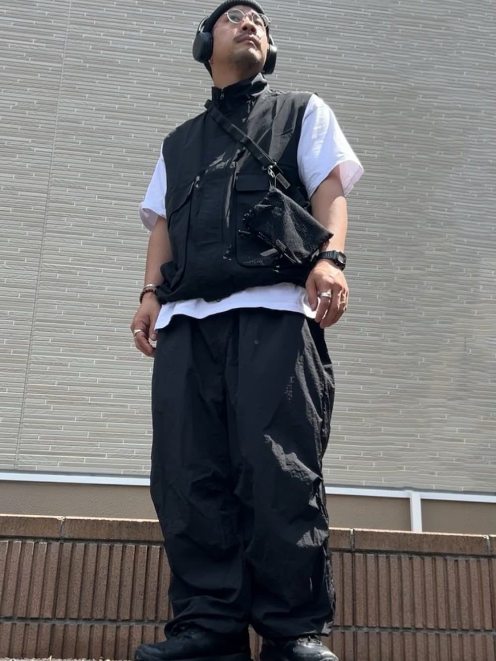 ブラック系のベスト、ブラック系のショルダーバッグ、ブラック系のカーゴパンツを着用したメンズの春コーディネートの2枚目の写真