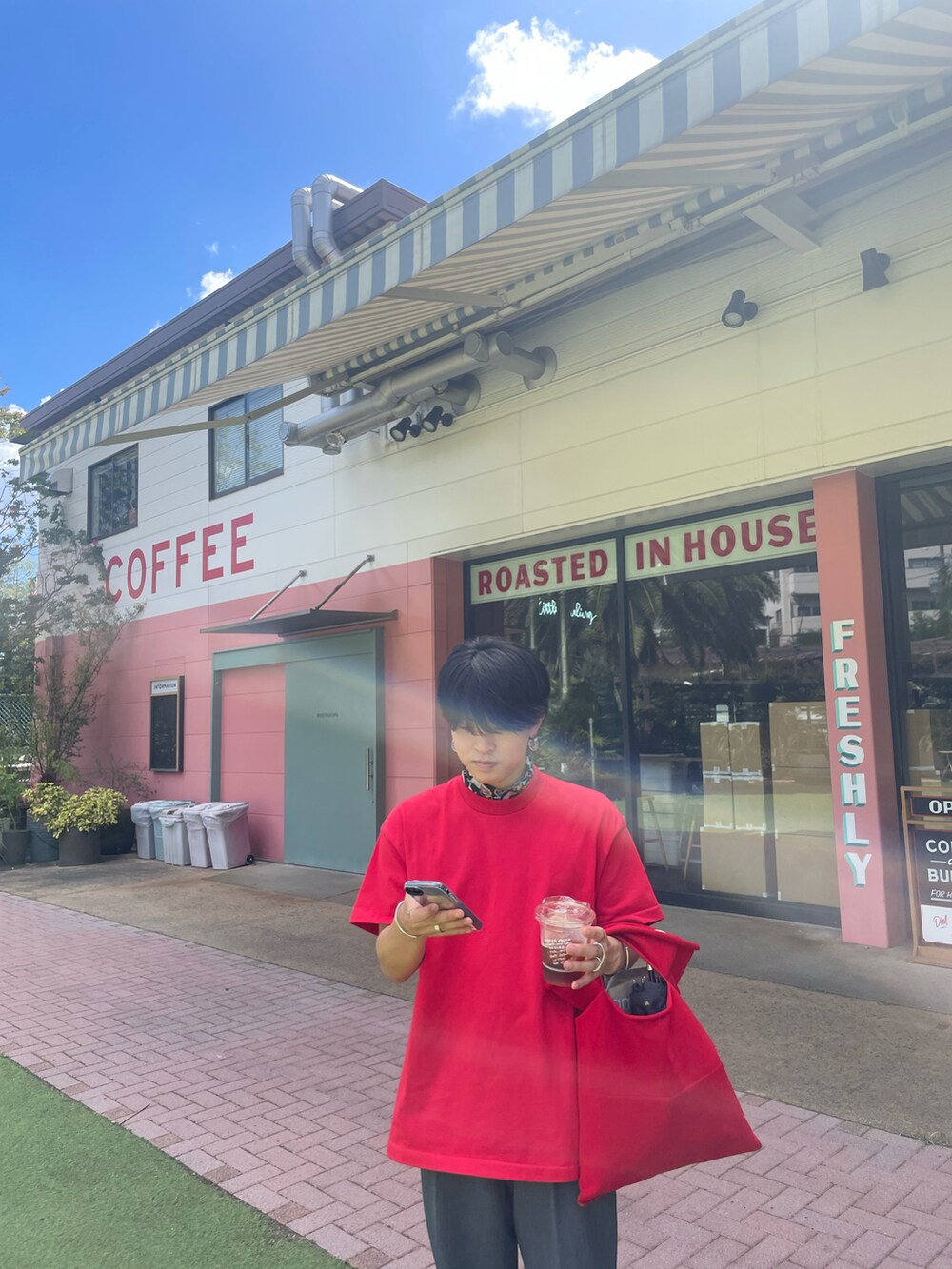 レッド系のTシャツ/カットソー、レッド系のハンドバッグ、ブラウン系のサングラスを着用したメンズの夏コーディネートの3枚目の写真