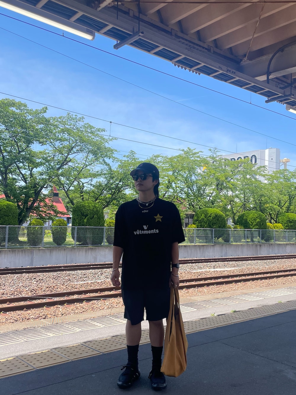 ブラック系のTシャツ/カットソー、イエロー系のバッグ、ブラック系のスニーカーを着用したメンズの夏コーディネートの2枚目の写真