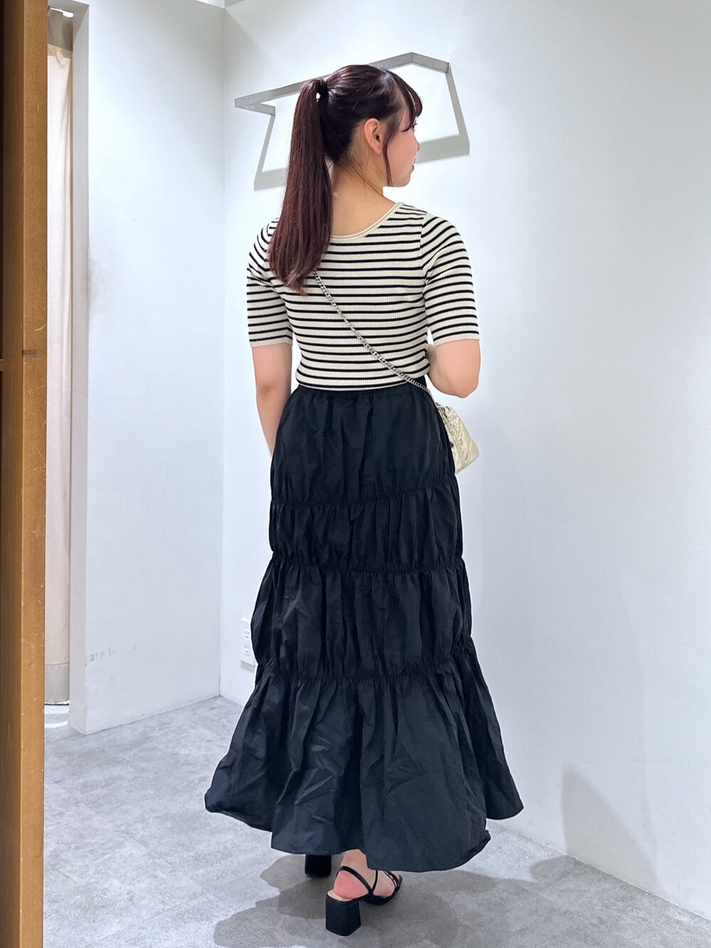 ブラック系のスカート、ゴールド系のショルダーバッグ、ホワイト系のニット/セーターを着用したレディースの春コーディネートの3枚目の写真