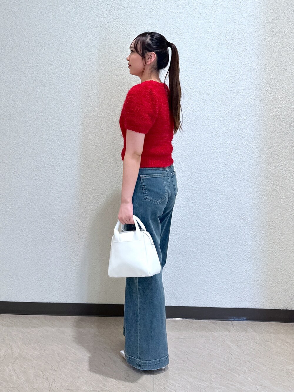 ブルー系のデニムパンツ、レッド系のニット/セーター、ホワイト系のトートバッグを着用したレディースの春コーディネートの2枚目の写真