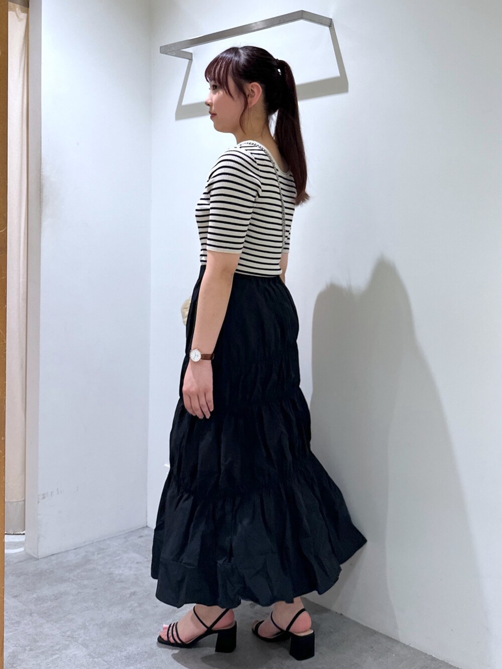 ブラック系のスカート、ゴールド系のショルダーバッグ、ホワイト系のニット/セーターを着用したレディースの春コーディネートの2枚目の写真