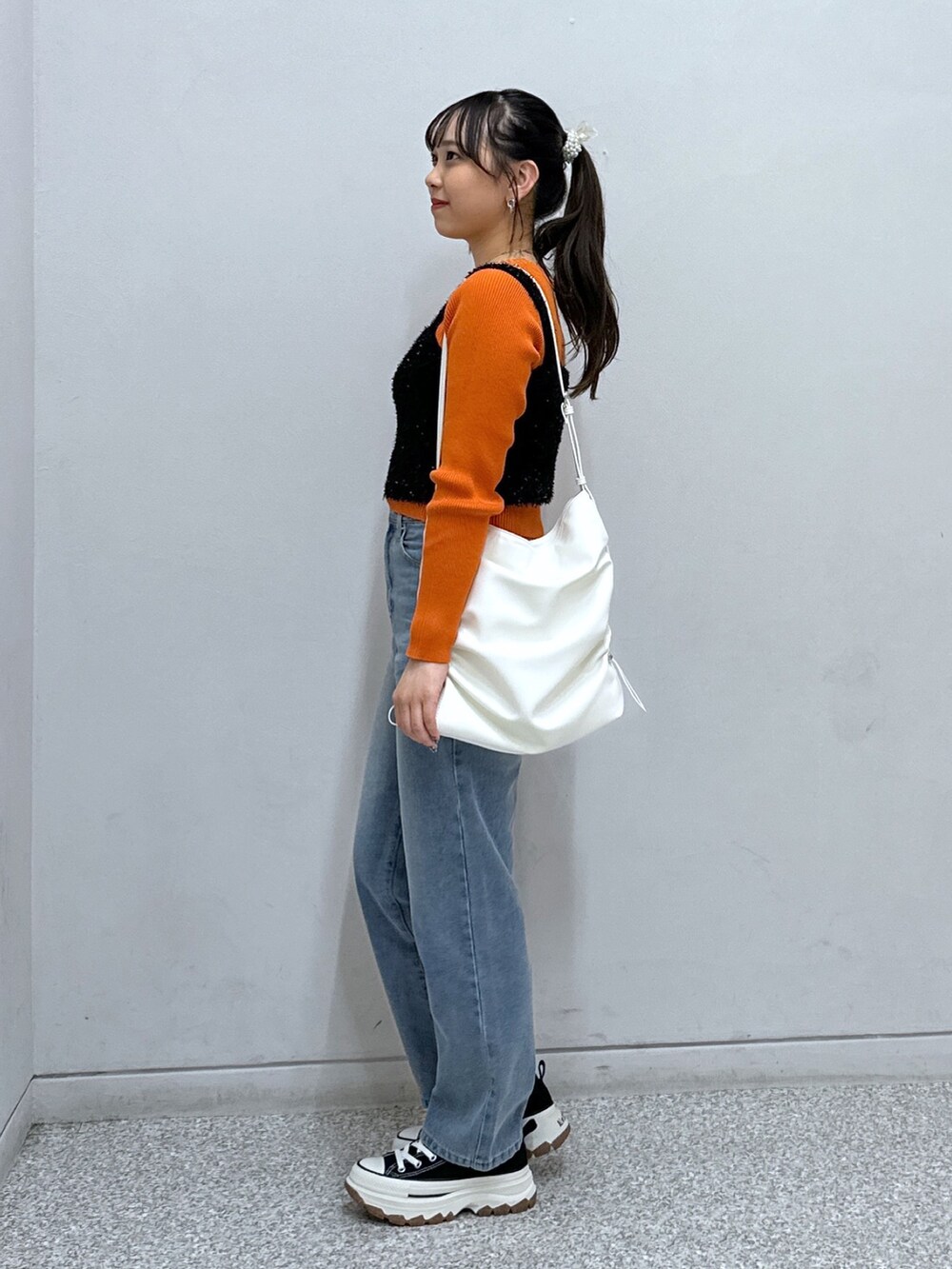 ブルー系のデニムパンツ、ホワイト系のトートバッグ、オレンジ系のニット/セーターを着用したレディースの秋コーディネートの3枚目の写真