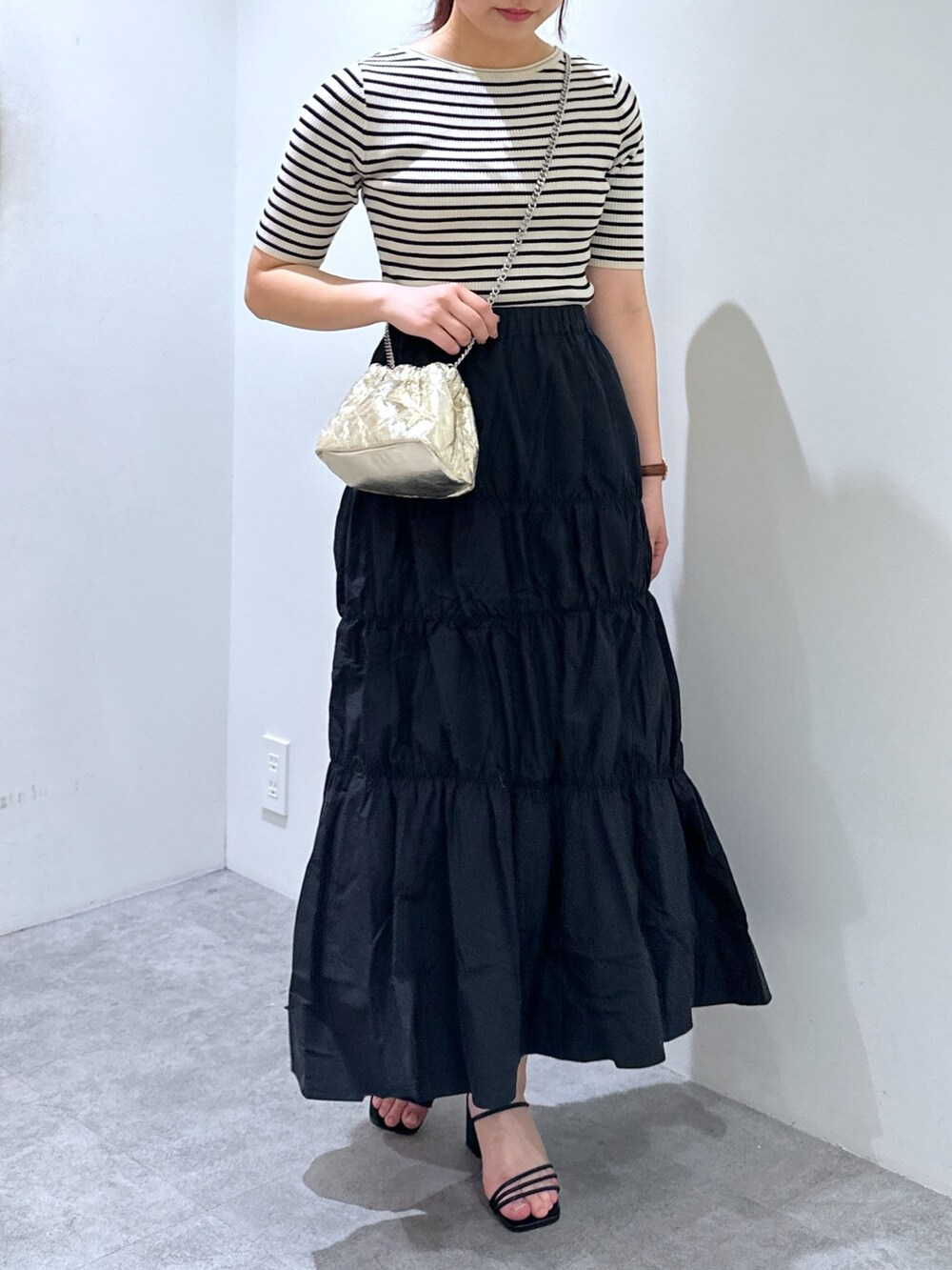 ブラック系のスカート、ゴールド系のショルダーバッグ、ホワイト系のニット/セーターを着用したレディースの春コーディネートの4枚目の写真