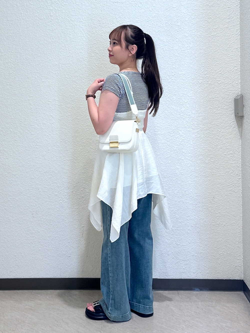 ホワイト系のワンピース、ブルー系のデニムパンツ、ブラック系のサンダルを着用したレディースの夏コーディネートの2枚目の写真