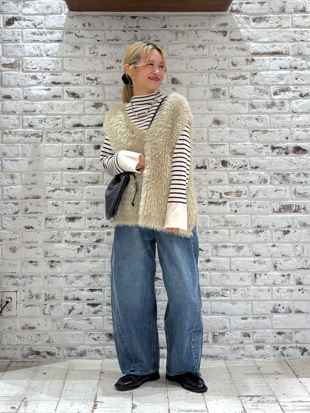 ブラック系のショルダーバッグ、ブルー系のデニムパンツ、ベージュ系のベストを着用したレディースの秋コーディネートの2枚目の写真