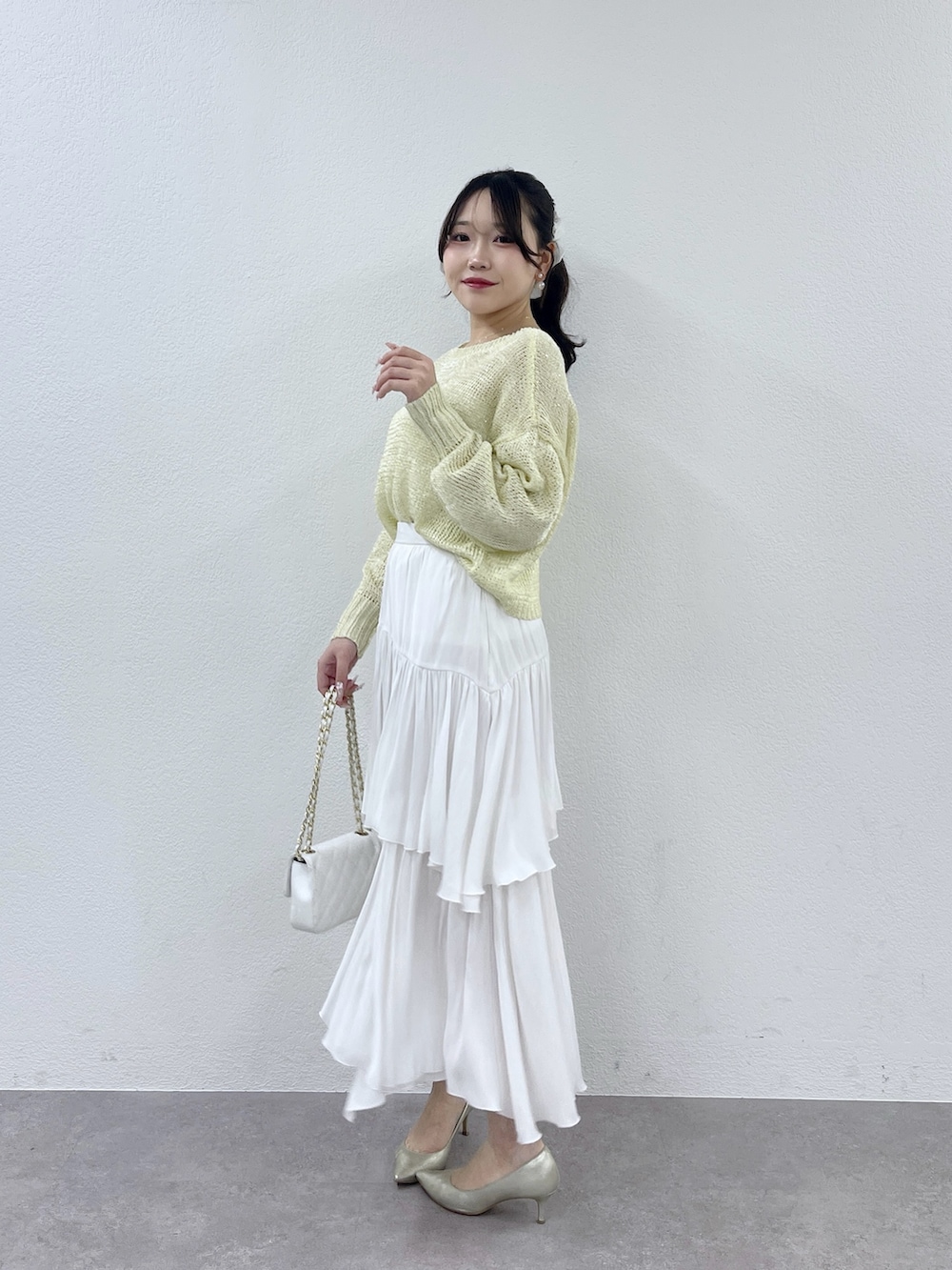 ホワイト系のハンドバッグ、ホワイト系のスカート、イエロー系のニット/セーターを着用したレディースの冬コーディネートの2枚目の写真