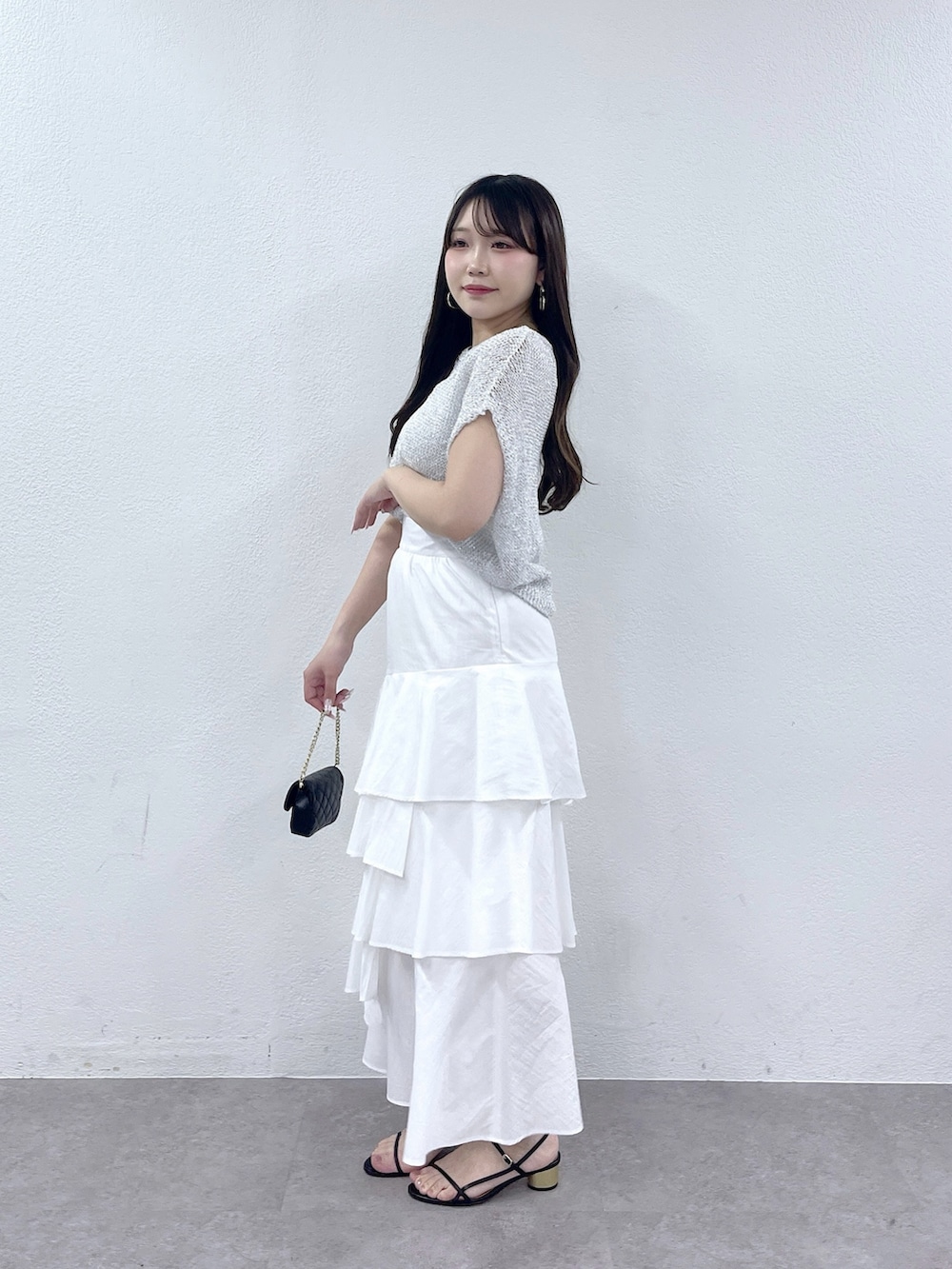 ホワイト系のスカート、シルバー系のニット/セーター、ブラック系のトートバッグを着用したレディースの春コーディネートの2枚目の写真