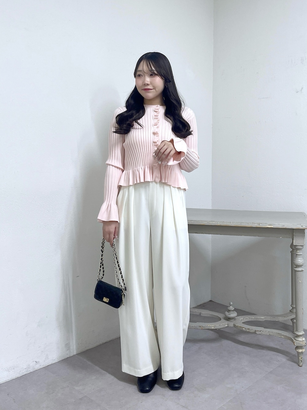 ピンク系のニット/セーター、ホワイト系のスラックス、ブラック系のブーツを着用したレディースの秋コーディネートの2枚目の写真