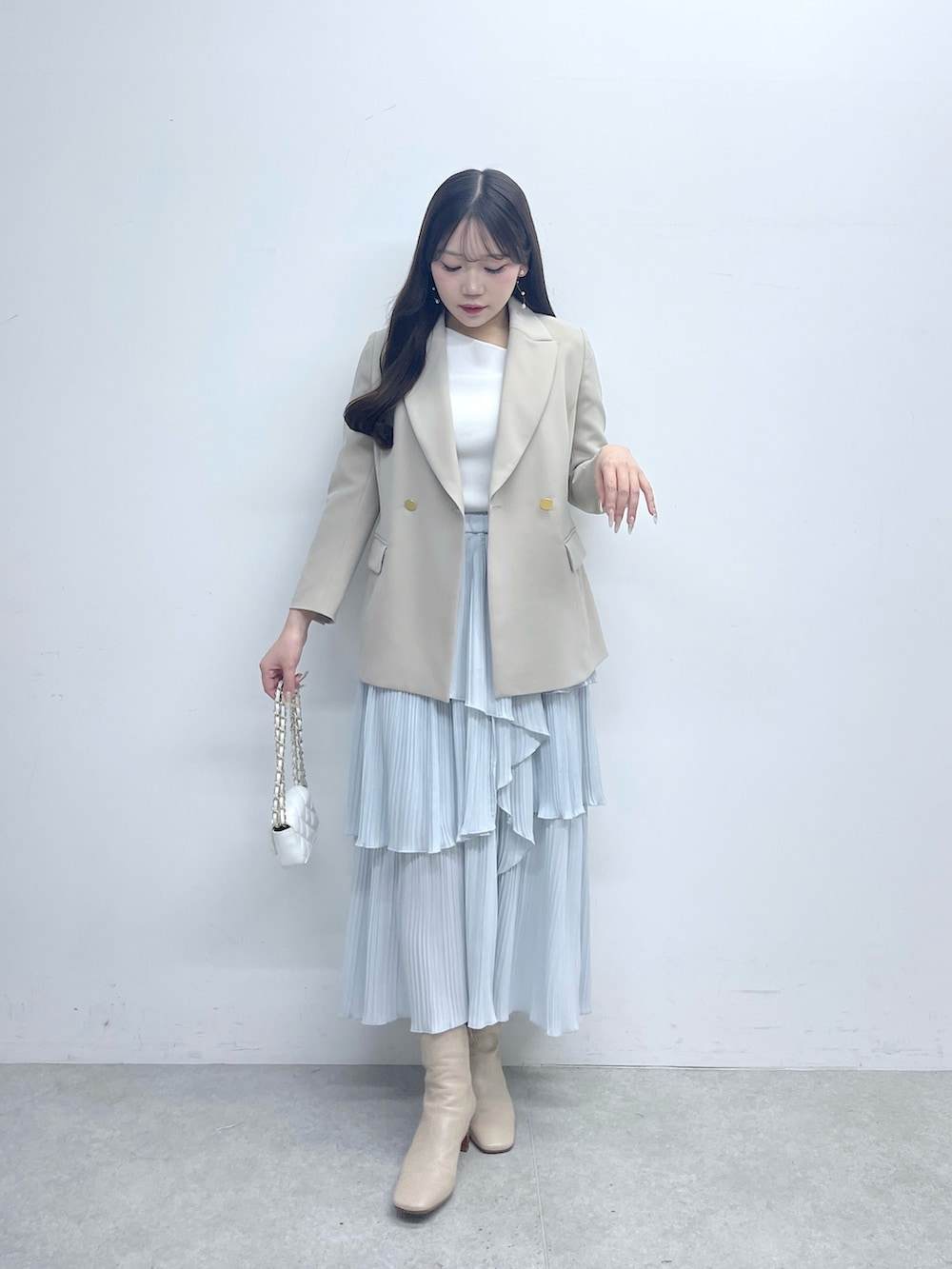 ベージュ系のテーラードジャケット、ホワイト系のニット/セーター、ブルー系のスカートを着用したレディースの春コーディネートの2枚目の写真