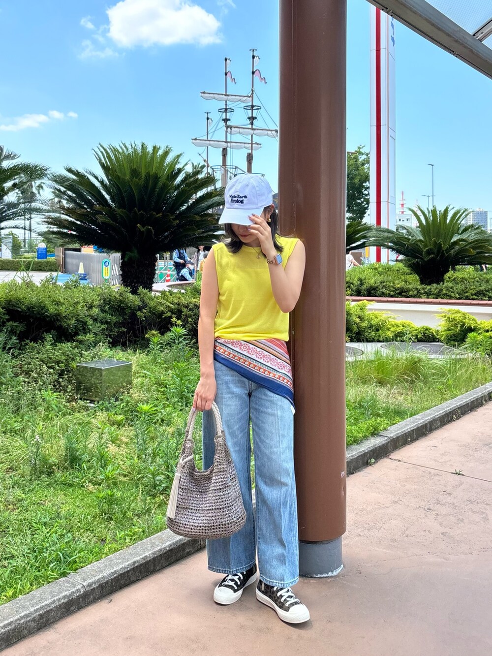 イエロー系のタンクトップ、ブルー系のデニムパンツ、ベージュ系のかごバッグを着用したレディースの夏コーディネートの2枚目の写真