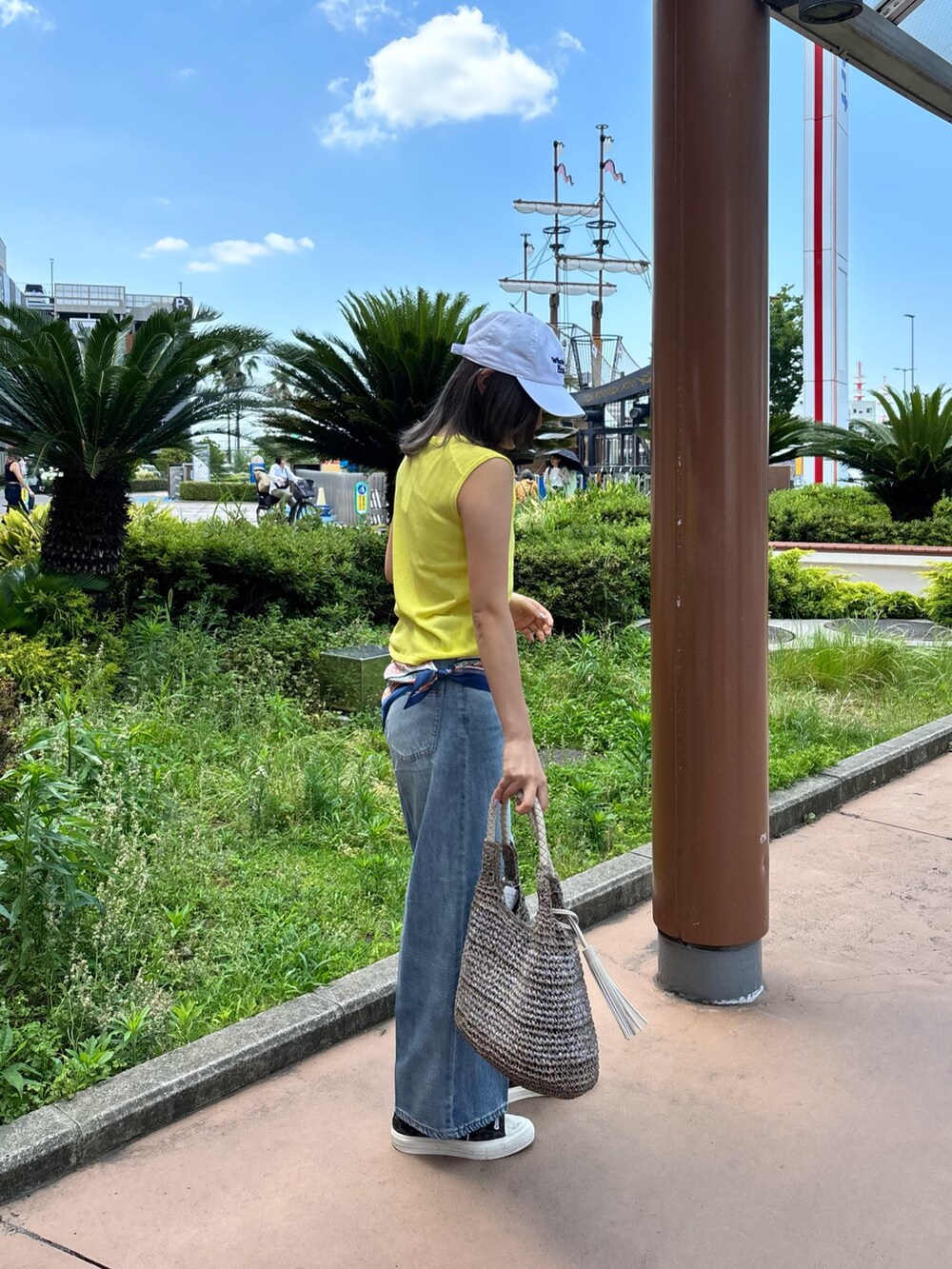 イエロー系のタンクトップ、ブルー系のデニムパンツ、ベージュ系のかごバッグを着用したレディースの夏コーディネートの3枚目の写真