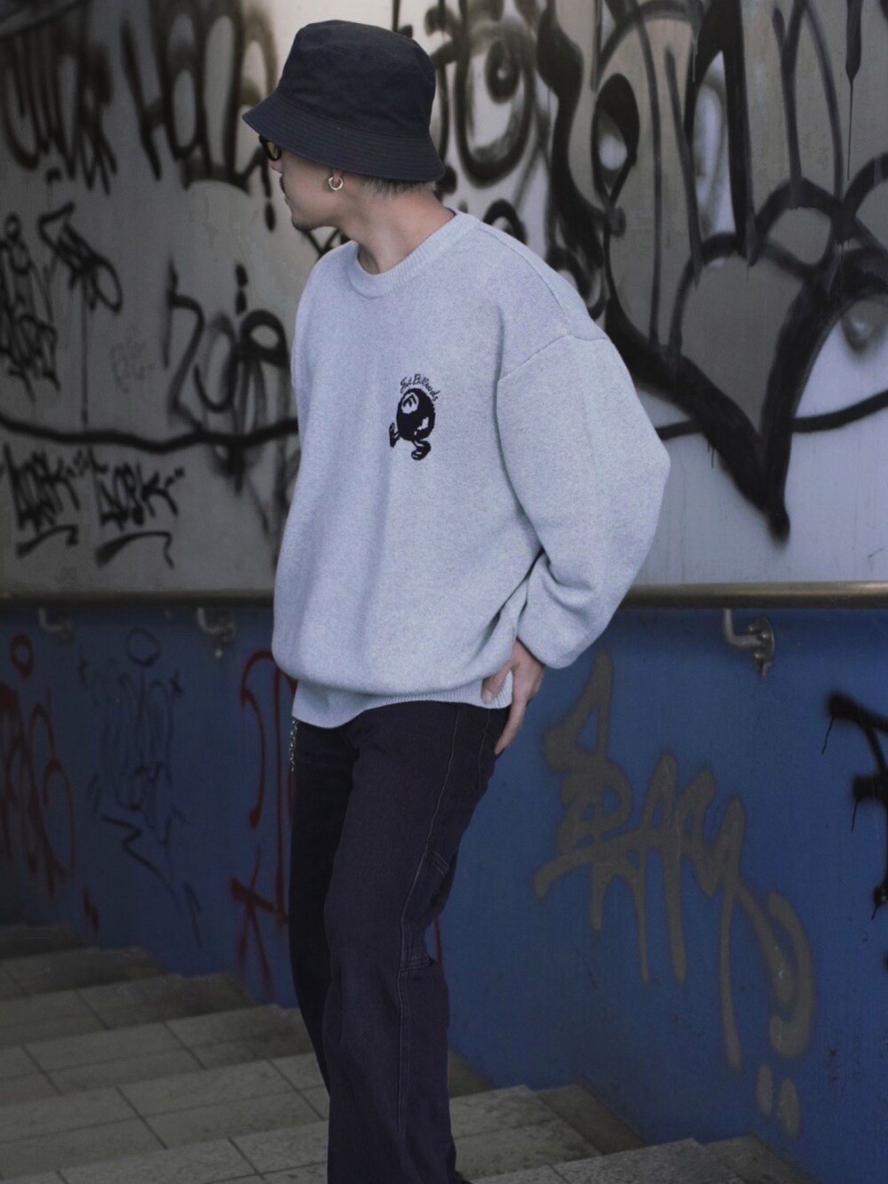 ブラック系のデニムパンツ、グレー系のニット/セーター、ブルー系のスニーカーを着用したメンズの冬コーディネートの2枚目の写真