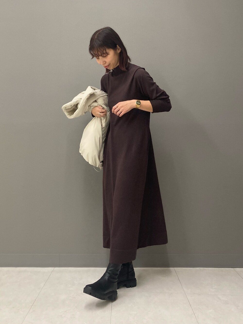 ブラウン系のワンピース、ブラック系のブーツ、ホワイト系のブルゾンを着用したレディースの冬コーディネートの2枚目の写真