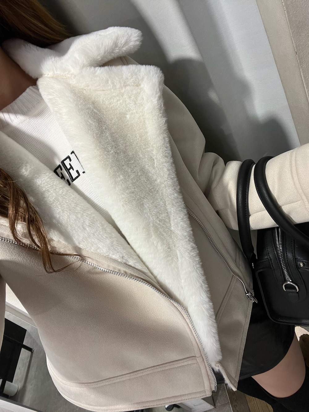 ホワイト系のムートンコート、ホワイト系のニット/セーター、ブラック系のスカートを着用したレディースの秋コーディネートの4枚目の写真