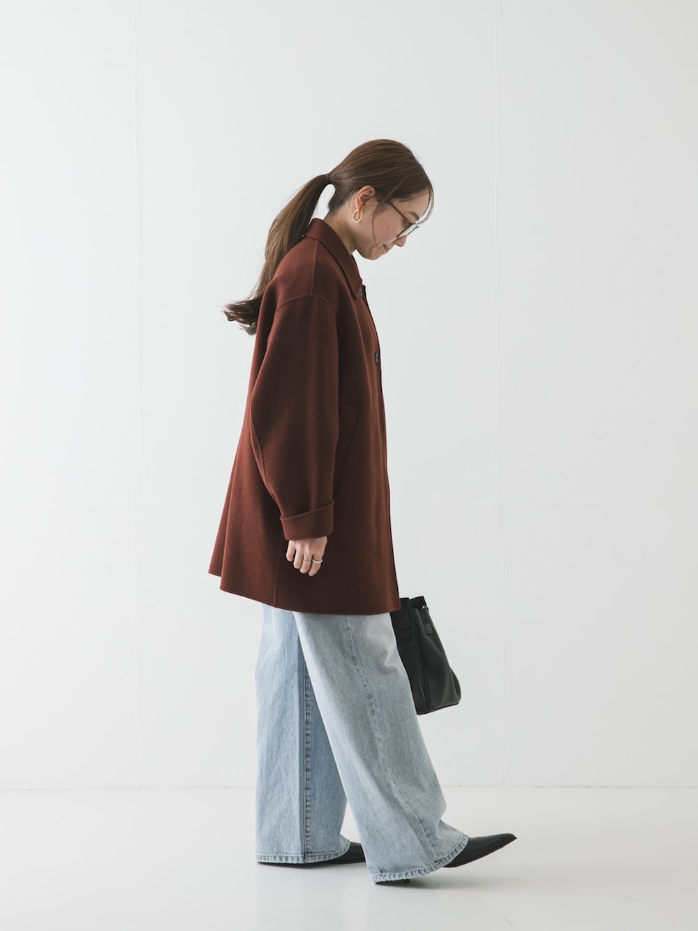 ブルー系のデニムパンツ、ブラウン系のステンカラーコート、ブラウン系のメガネを着用したレディースの冬コーディネートの3枚目の写真