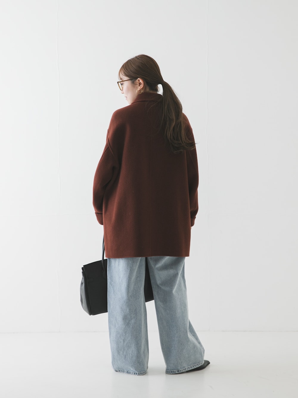 ブルー系のデニムパンツ、ブラウン系のステンカラーコート、ブラウン系のメガネを着用したレディースの冬コーディネートの2枚目の写真