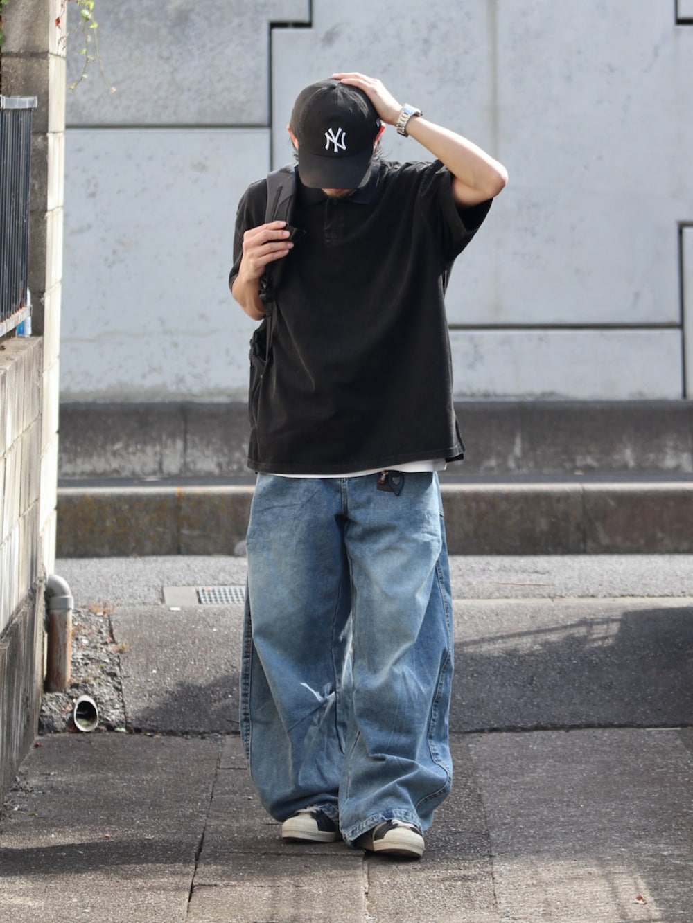 ブルー系のデニムパンツ、ブラック系のポロシャツ、シルバー系のピアス（片耳用）を着用したメンズの夏コーディネートの2枚目の写真