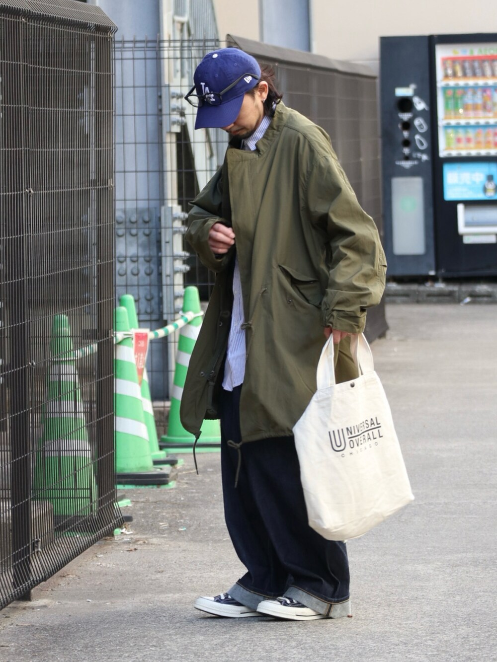 グリーン系のミリタリージャケット、ホワイト系のトートバッグ、ブルー系のキャップを着用したメンズの春コーディネートの2枚目の写真