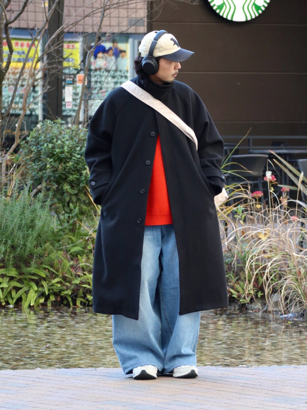 オレンジ系のニット/セーター、ブラック系のステンカラーコート、ブルー系のデニムパンツを着用したメンズの冬コーディネートの2枚目の写真