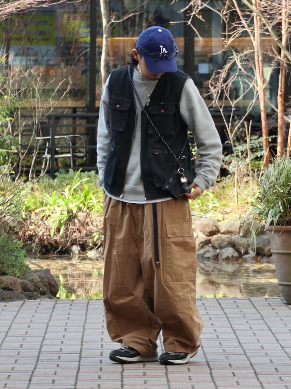 ベージュ系のカーゴパンツ、ブラック系のベスト、ブルー系のキャップを着用したメンズの春コーディネートの2枚目の写真