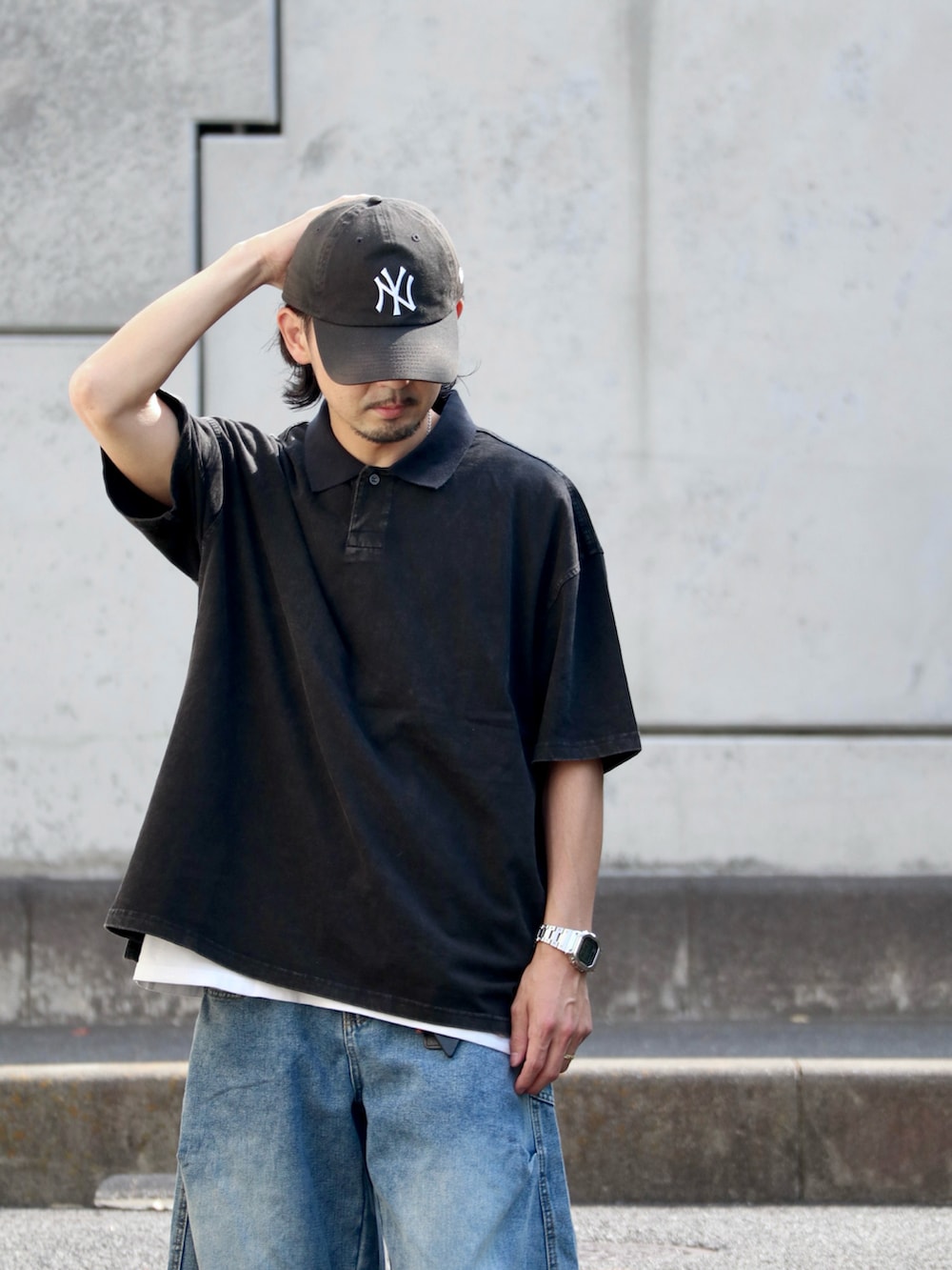 ブルー系のデニムパンツ、ブラック系のポロシャツ、シルバー系のピアス（片耳用）を着用したメンズの夏コーディネートの3枚目の写真