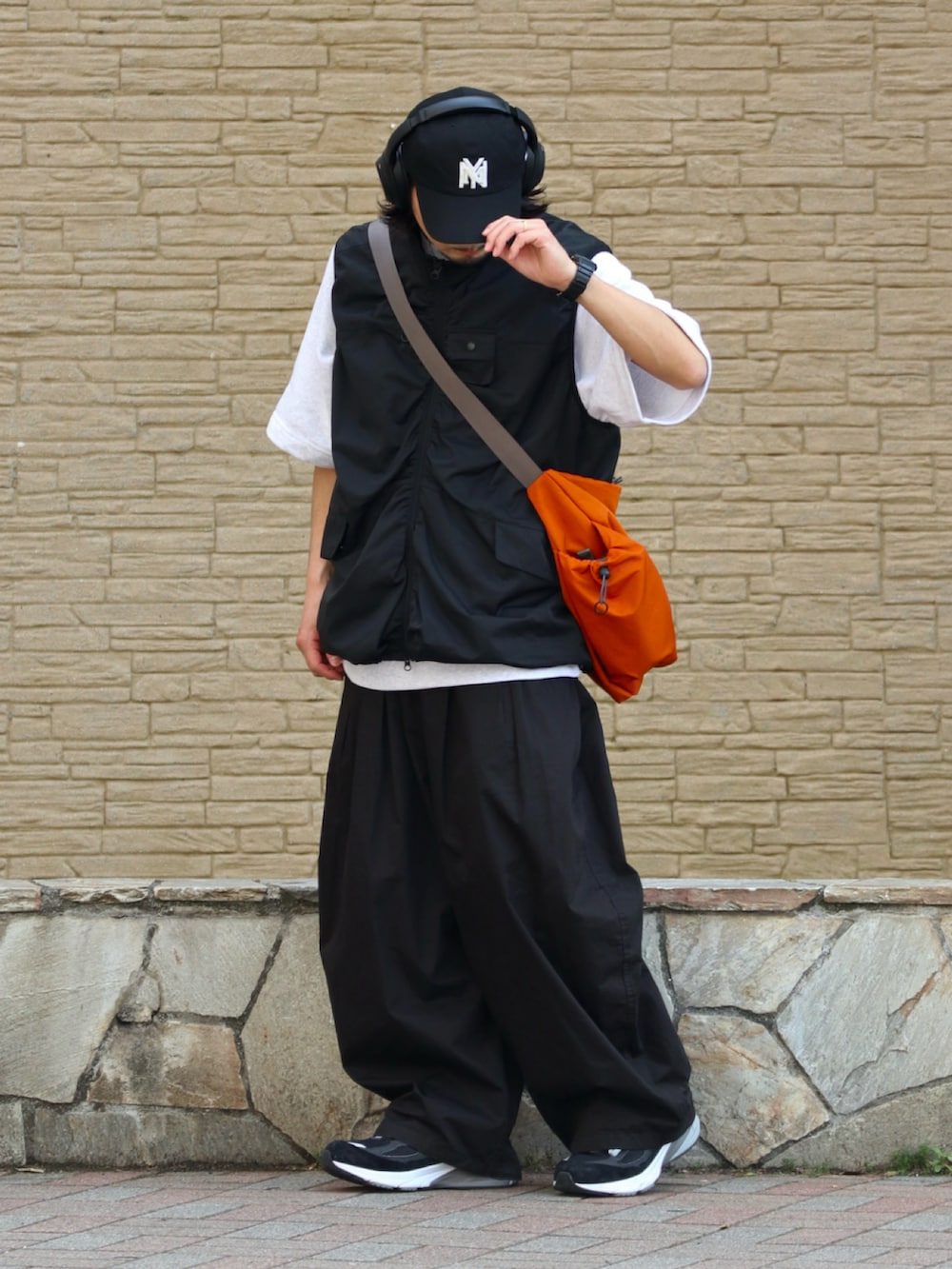 オレンジ系のショルダーバッグ、グレー系のTシャツ/カットソー、ブラック系のチノパンツを着用したメンズの夏コーディネートの2枚目の写真