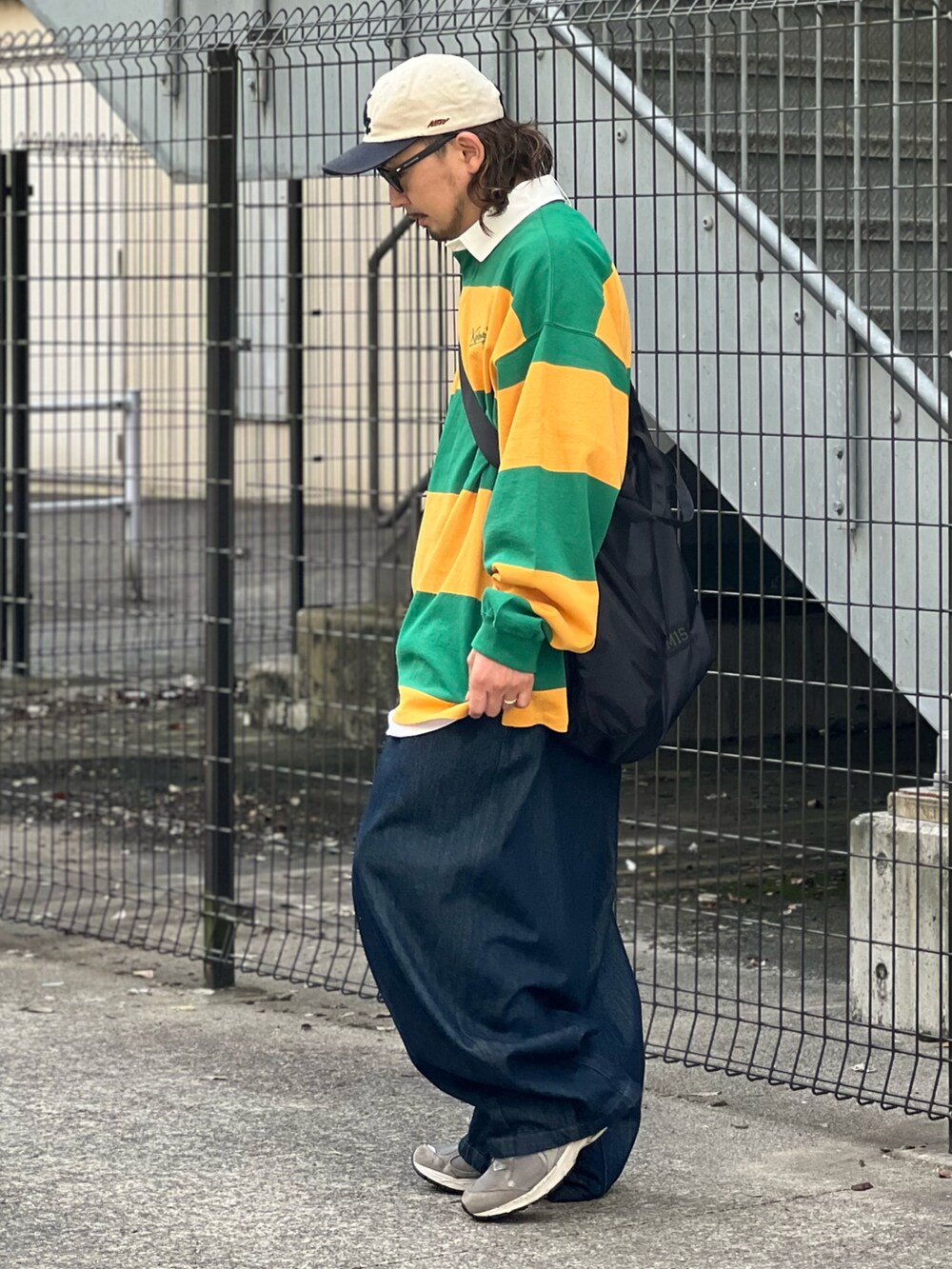 イエロー系のポロシャツ、ブルー系のデニムパンツ、ブラック系のショルダーバッグを着用したメンズの秋コーディネートの2枚目の写真