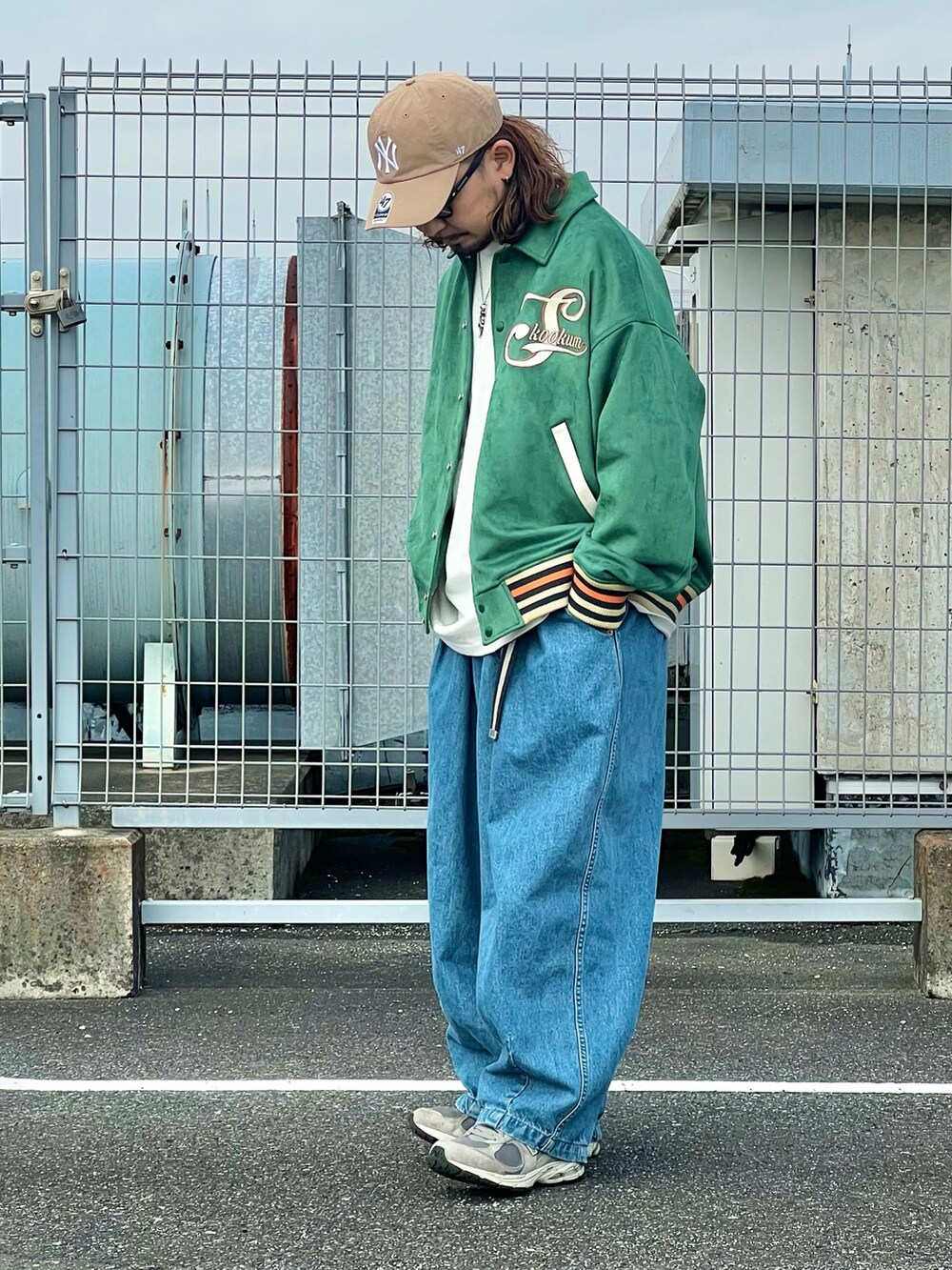 グリーン系のスタジャン、ブルー系のデニムパンツ、ベージュ系のキャップを着用したメンズの春コーディネートの2枚目の写真