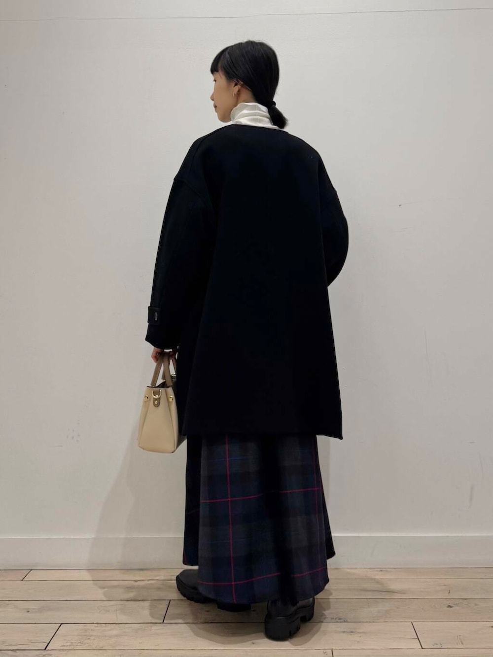 ホワイト系のトートバッグ、ブラック系のノーカラーコート、ブラック系のブーツを着用したレディースの冬コーディネートの3枚目の写真