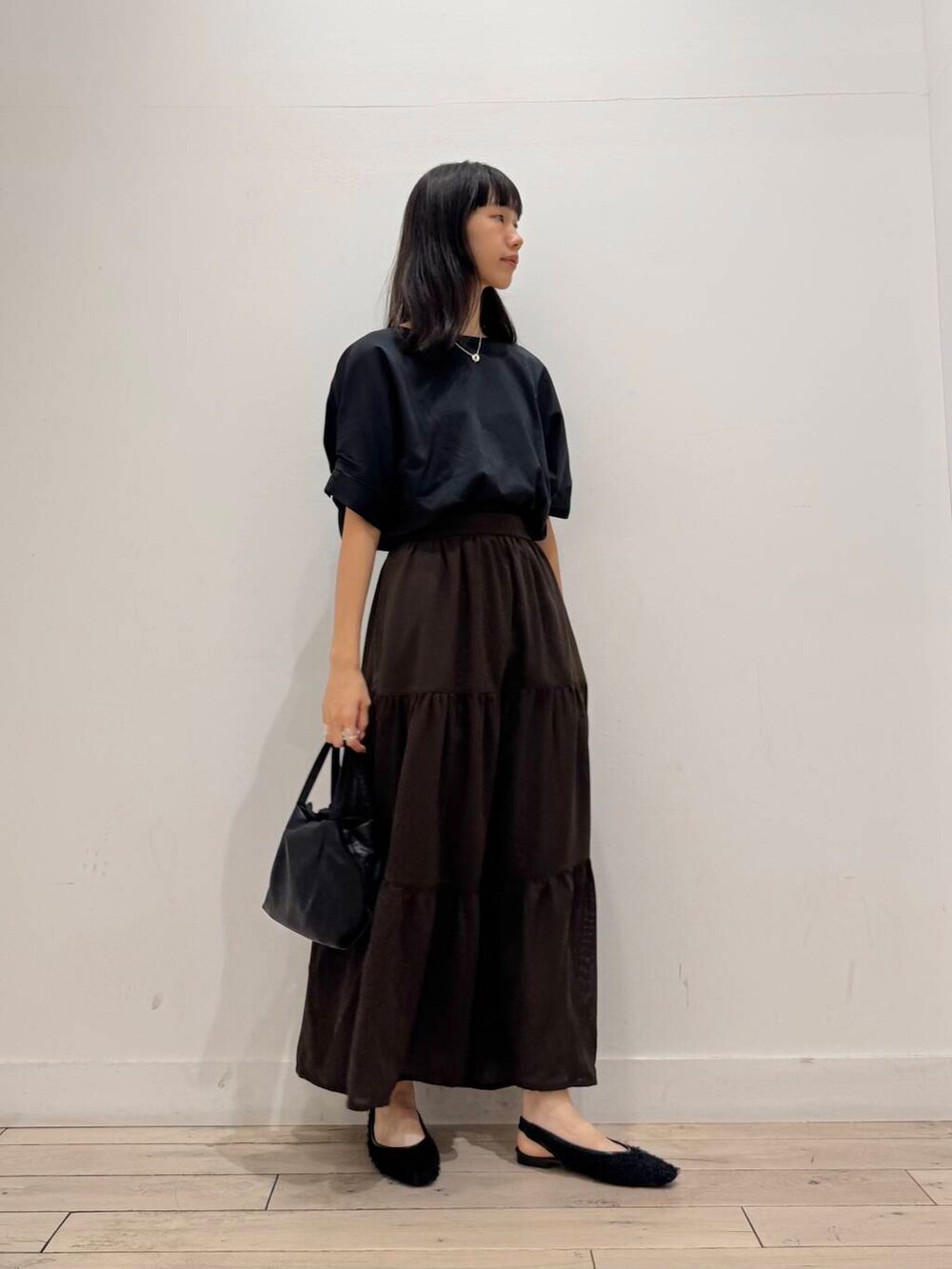 ブラック系のショルダーバッグ、ブラック系のTシャツ/カットソー、ブラウン系のスカートを着用したレディースの夏コーディネートの2枚目の写真