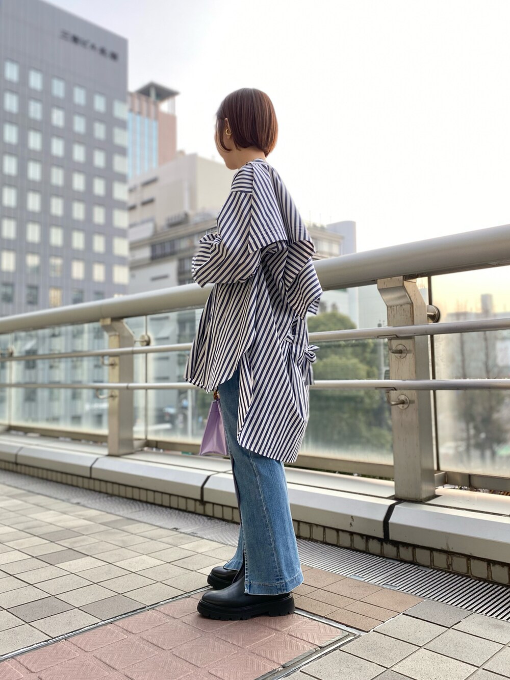 パープル系のハンドバッグ、ブルー系のシャツ/ブラウス、ブルー系のデニムパンツを着用したレディースの春コーディネートの2枚目の写真